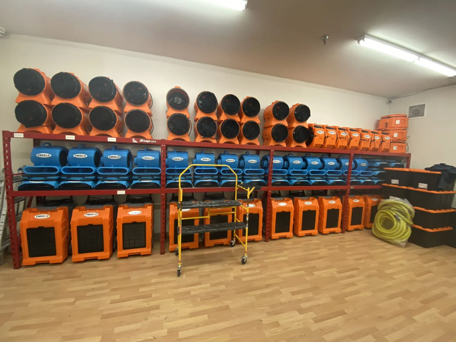 Rows of commercial dehumidifiers and air movers staged in the Emer C warehouse